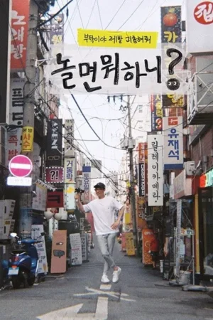 Um homem jovem e sorridente numa rua movimentada da cidade, segurando uma câmera de selfie. A atmosfera é vibrante e urbana, com muitos sinais em coreano e um visual geral colorido.