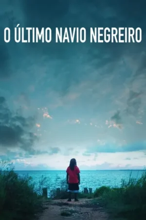 Criança/jovem de costas em um caminho de terra, olhando o vasto mar azul-turquesa sob um céu nublado. Vegetação na costa.