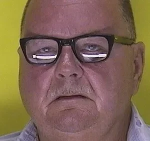 Close-up de um homem de meia-idade usando óculos, com fundo amarelo vibrante. Expressão séria. Espero que isso ajude!