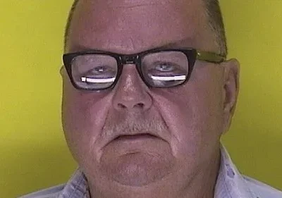 Close-up de um homem de meia-idade usando óculos, com fundo amarelo vibrante. Expressão séria. Espero que isso ajude!