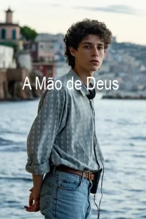 Um jovem de cabelo cacheado e fones no pescoço, camisa azul e jeans, olha pensativo à beira-mar, com uma cidade mediterrânea ao fundo.