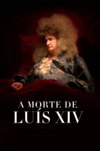 Homem idoso com cabelo grisalho e volumoso, vestido com robe azul decorado, sentado em leito vermelho. Fundo escuro e sombrio.