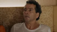 Homem suado,de meia-idade,com olhos arregalados e boca aberta,expressando choque ou medo. Usa camiseta branca.