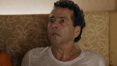Babilônia – T01E111:Capítulo 111 1 Homem suado,de meia-idade,com olhos arregalados e boca aberta,expressando choque ou medo. Usa camiseta branca.