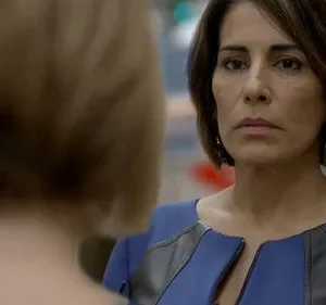 Mulher de cabelo escuro e vestido azul encara seriamente outra pessoa de costas, cabelo claro. Foco intenso e atmosfera dramática.