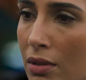 Close-up de mulher com olhar pensativo, brinco brilhante. Fundo escuro desfocado. Clima sério e introspectivo.