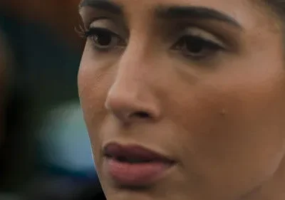 Close-up de mulher com olhar pensativo, brinco brilhante. Fundo escuro desfocado. Clima sério e introspectivo.