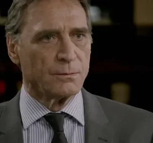 Homem de terno, cabelos grisalhos, com olhar sério e focado. Fundo escuro e formal, com um tom de suspense.