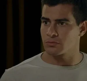 Jovem de camisa cinza, olhar intenso e concentrado para a esquerda. Fundo escuro, sugere ambiente sério ou reflexivo.