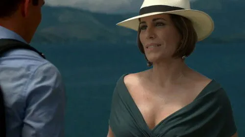 Babilônia – T01E15:Capítulo 15 1 Uma mulher de chapéu e vestido verde olha para um homem de costas,com o mar azul ao fundo. Cenário costeiro e clima de verão.