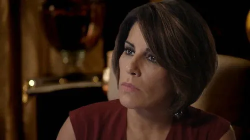 Babilônia – T01E21:Capítulo 21 1 Close-up de mulher com cabelo castanho-escuro e olhar intenso,usando blusa bordô,em ambiente escuro e dramático.