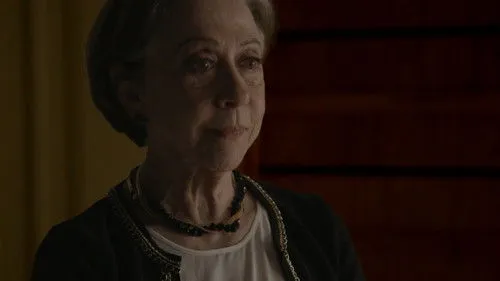 Mulher idosa de cabelo grisalho com olhar contemplativo. Veste casaco escuro,colar. Fundo sombrio e texturizado.