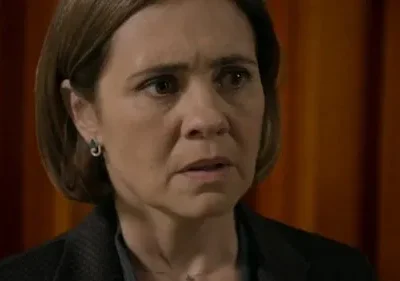 Close-up de mulher de meia-idade com expressão preocupada e cabelo castanho, contra um fundo desfocado de tons quentes.