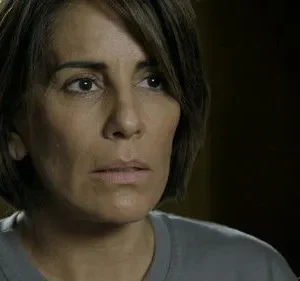 Close-up de mulher com cabelo castanho curto e expressão preocupada. Ela olha para o lado contra fundo escuro.