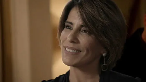 Babilônia – T01E50:Capítulo 50 1 Mulher de cabelo curto sorri,olhando gentilmente para o lado. Fundo interno desfocado com tons quentes e suaves.
