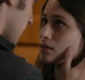 Close-up de mulher com expressão intensa olhando para um homem, que toca seu rosto. Clima íntimo e emocional.