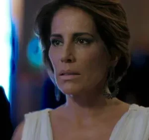 Mulher de cabelo curto, vestido branco e expressão preocupada. Fundo escuro com luzes azuis intensas. Clima misterioso.