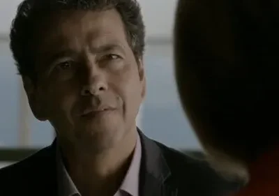 Homem de meia-idade, cabelo escuro e sorriso sutil, veste paletó e olha para o lado em ambiente com luz suave.