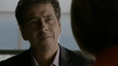 Homem de meia-idade,cabelo escuro e sorriso sutil,veste paletó e olha para o lado em ambiente com luz suave.