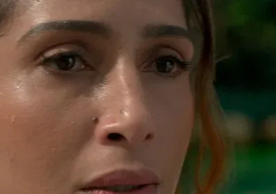 Close-up de mulher com pele suada, piercings no nariz e olhar sério. Fundo verde borrado. Atmosfera tensa.