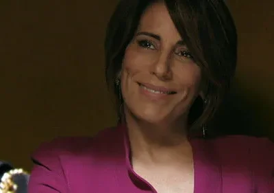 Mulher de cabelo castanho e blazer magenta sorri gentilmente. Fundo escuro e discreto, com um toque de elegância no ambiente.