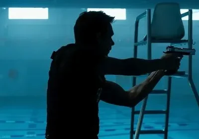 Homem em silhueta mira arma em piscina escura e azulada com cadeira de salva-vidas. Ambiente misterioso e tenso.