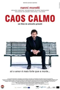 Homem de terno escuro e barba sentado em banco nevado,olhando para frente. Cenário minimalista,de inverno,com clima sombrio.