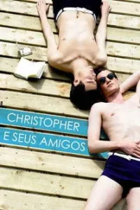 Dois homens em roupa de banho relaxam em um deque de madeira. Um de bruços,outro de costas com óculos de sol. Clima de verão.