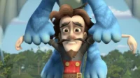 Homem de bigode e barba, visivelmente assustado, é segurado no ar pela mão de um grande monstro azul peludo. Cenário de floresta e céu.