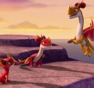 Três dragões animados num penhasco costeiro. Um laranja voa sobre o mar, dois vermelhos menores nas rochas. Céu de pôr do sol.