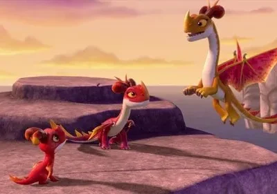 Três dragões animados num penhasco costeiro. Um laranja voa sobre o mar, dois vermelhos menores nas rochas. Céu de pôr do sol.