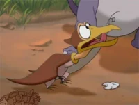 Pterodáctilo animado, marrom, com bico amarelo, língua para fora e olhos arregalados. Ele parece tonto no chão árido com um dente branco.