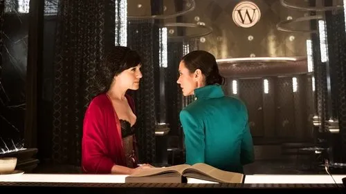 Expresso do Amanhã – T01E05:A justiça não embarcou 1 Duas mulheres em cenário luxuoso e escuro. Uma de vermelho,outra de verde-água,conversam seriamente sobre um livro.