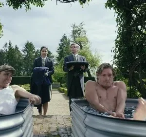 Dois homens em banhos de gelo em tinas no jardim. Um sorri, o outro parece gelado. Criados os servem.