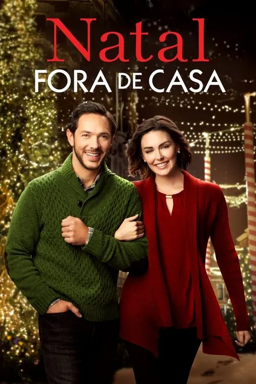 Casal sorridente em cenário natalino noturno. Ele de suéter verde,ela de vermelho. Fundo iluminado por luzes cintilantes e árvores.