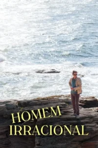 Homem de óculos e jaqueta em rochas escuras,de frente para o mar. O oceano é agitado e brilhante,sob o sol intenso.