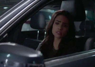 Close de mulher jovem morena com expressão séria dentro de um carro escuro. Ambiente noturno ou estacionamento.