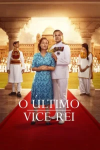 Casal formal no tapete vermelho;ele de uniforme militar,ela de vestido azul. Dois indianos nas laterais. Fundo:palácio e guarda militar.