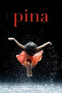 Dançarina de vestido coral salta na chuva contra um fundo escuro,com água espirrando ao redor.