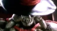 Criatura bizarra de pele escura e dentes afiados, carregando um objeto metálico gigante, em ambiente sombrio com tons vermelhos.