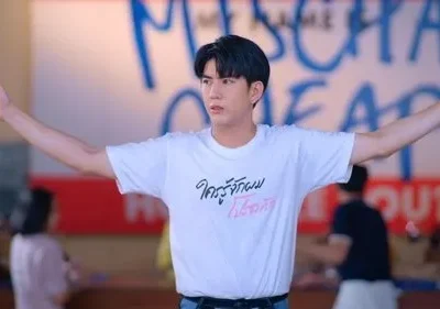 Jovem asiático com camiseta branca e braços abertos num local casual. Fundo tem graffiti azul. Cena vibrante e expressiva.