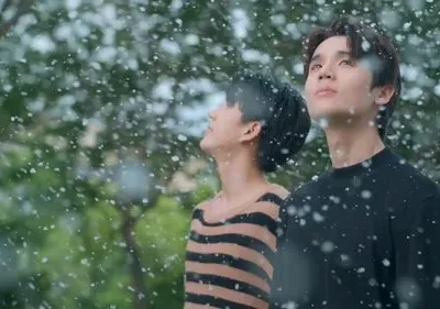 Dois jovens olham para cima enquanto flocos brancos caem suavemente. Ambiente exterior verde e calmo.