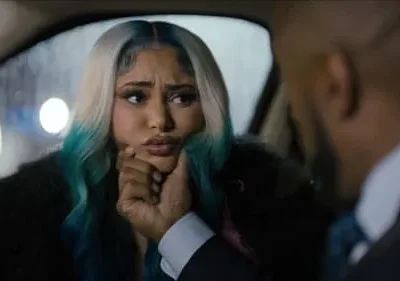 Mulher de cabelo loiro/azul com casaco de pele tem expressão apreensiva enquanto homem de terno segura seu queixo dentro de um carro à noite.