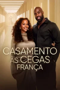Mulher e homem negros sorrindo, ele de camisa preta, ela de vestido champanhe. Ao fundo, corredor dourado e silhueta de casal.
