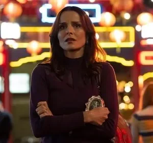 Mulher com expressão preocupada segura foto, em rua noturna iluminada por lanternas e luzes de neon. Ambiente vibrante, clima tenso.