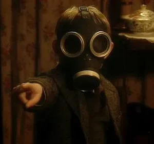 Criança com máscara de gás aponta para frente em sala escura e antiga. Ambiente misterioso e perturbador.