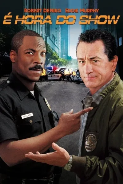 Dois homens se encaram: um policial negro e um civil branco. Apontam um para o outro, com fundo de carros policiais em chamas numa cidade.