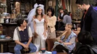 Noiva sorridente em vestido branco e véu entre amigos em um café. Ambiente acolhedor e descontraído com o grupo reunido.