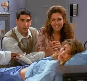 Médica faz ultrassom em mulher deitada na maca. Um homem observa preocupado, enquanto outra mulher sorri. Cenário de clínica médica com expectativa.