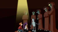 Três personagens (2 humanos, 1 robô) observam cinco figuras alienígenas encapuzadas em um palco escuro. Um feixe de luz foca uma das figuras.